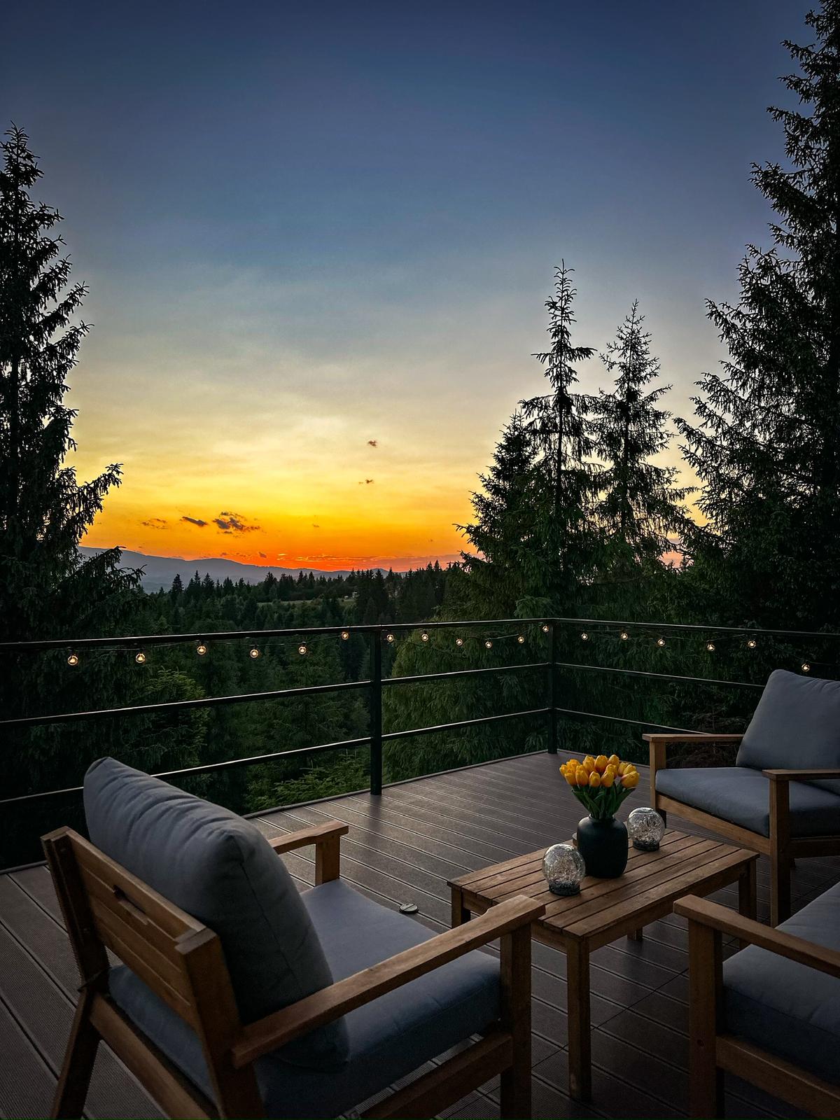 Sunset view from cabin deck with outdoor furniture overlooking forested mountains
