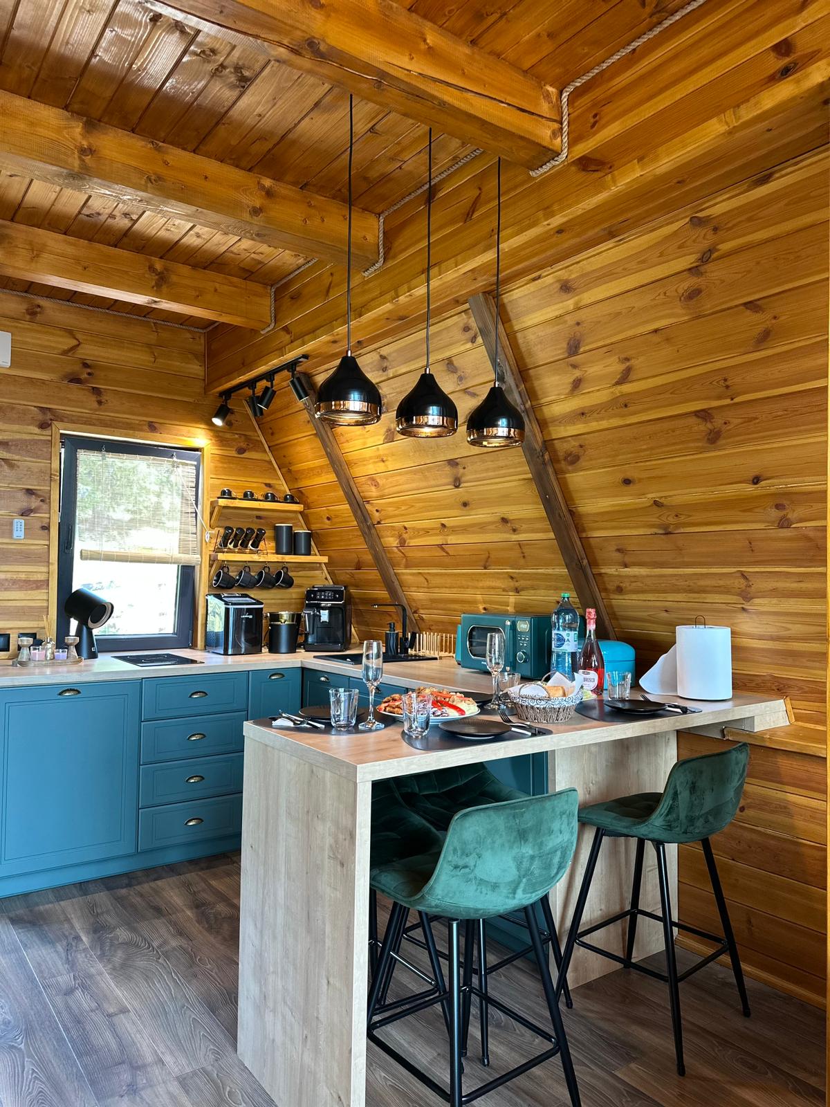 A-frame kitchen with teal cabinets, breakfast bar with velvet green chairs, pendant lights, and fully stocked amenities